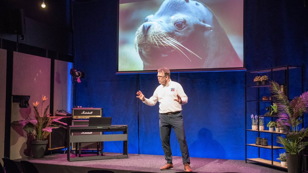 Robert van Schie op het podium, met een zeeleeuw op het scherm